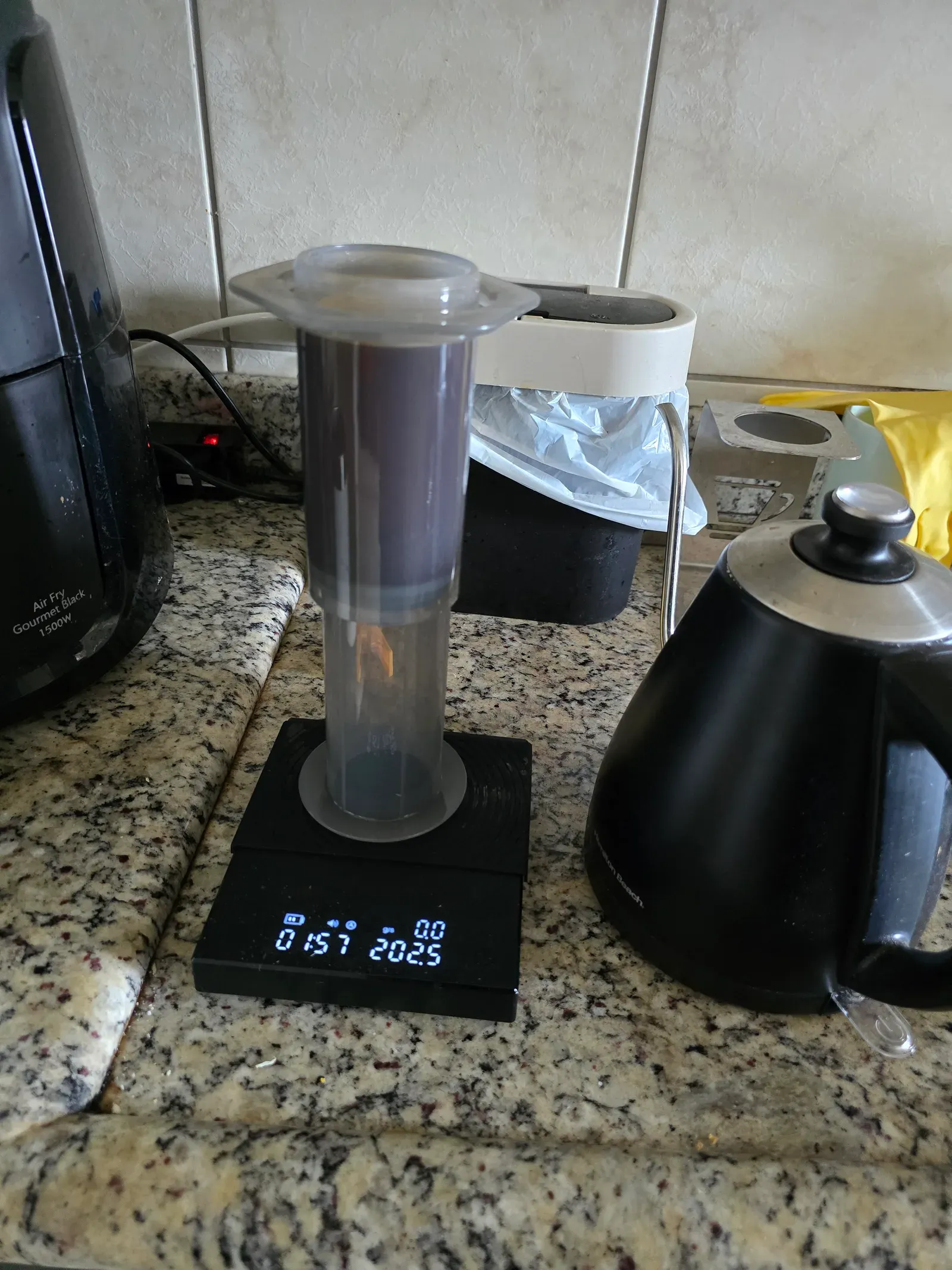 AeroPress brewing on a scale reading 202.5 g at 0:57, with a gooseneck kettle beside it on the kitchen counter