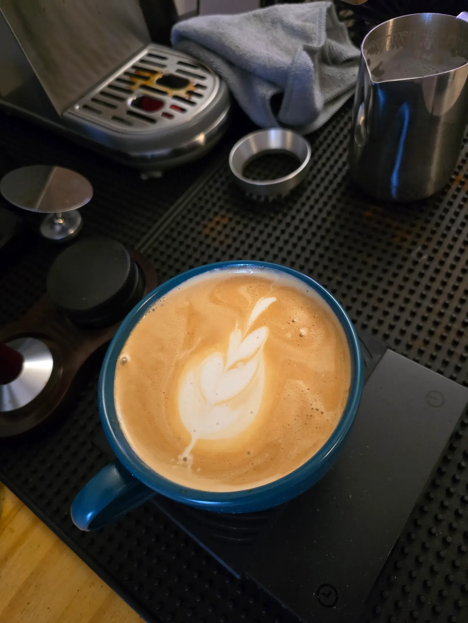 Latte in a teal cup with a three-layer tulip, milk pitcher and portafilter basket in the background
