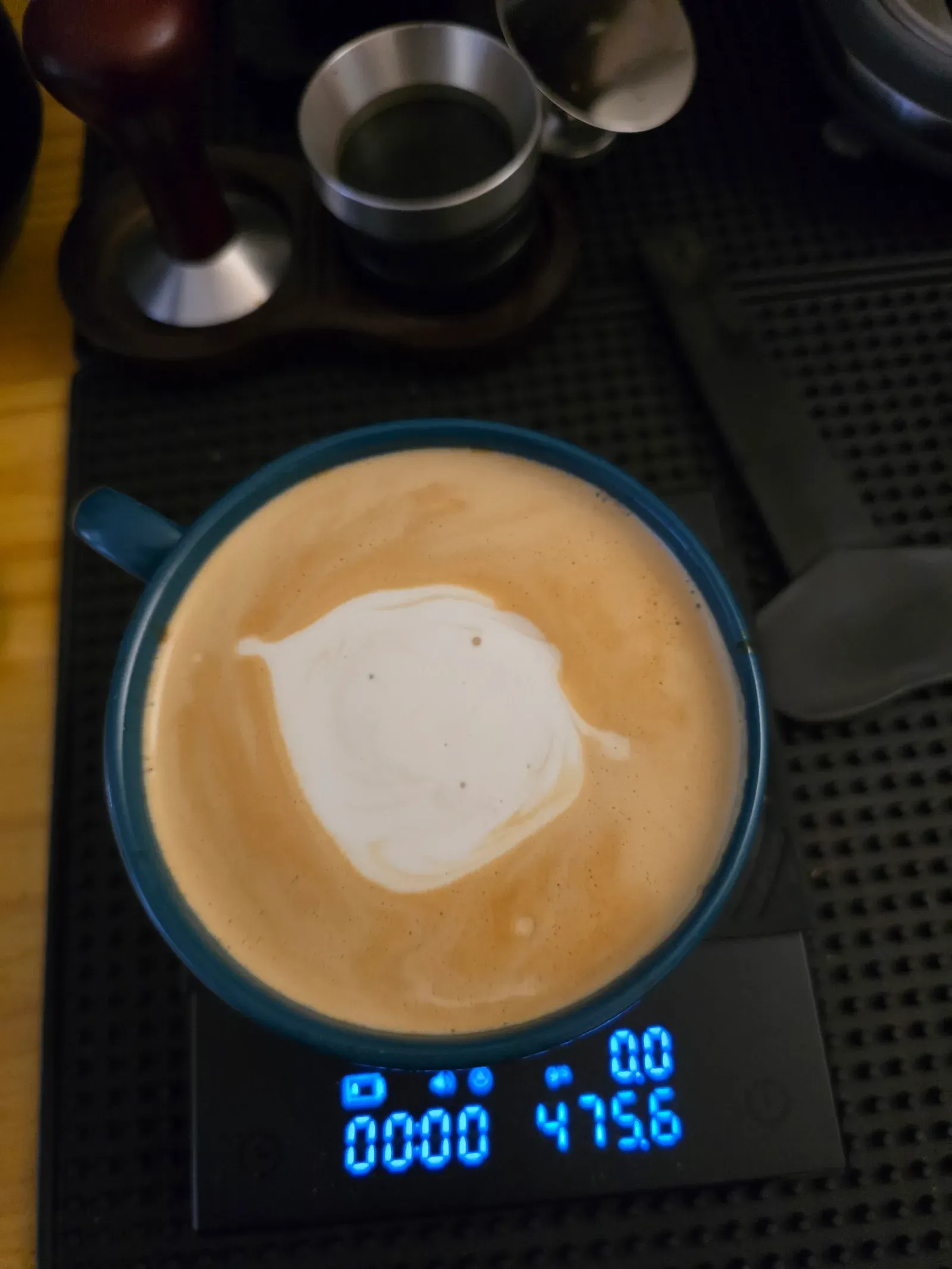 Latte in a teal cup with an early latte art attempt: a single white blob of milk in the center